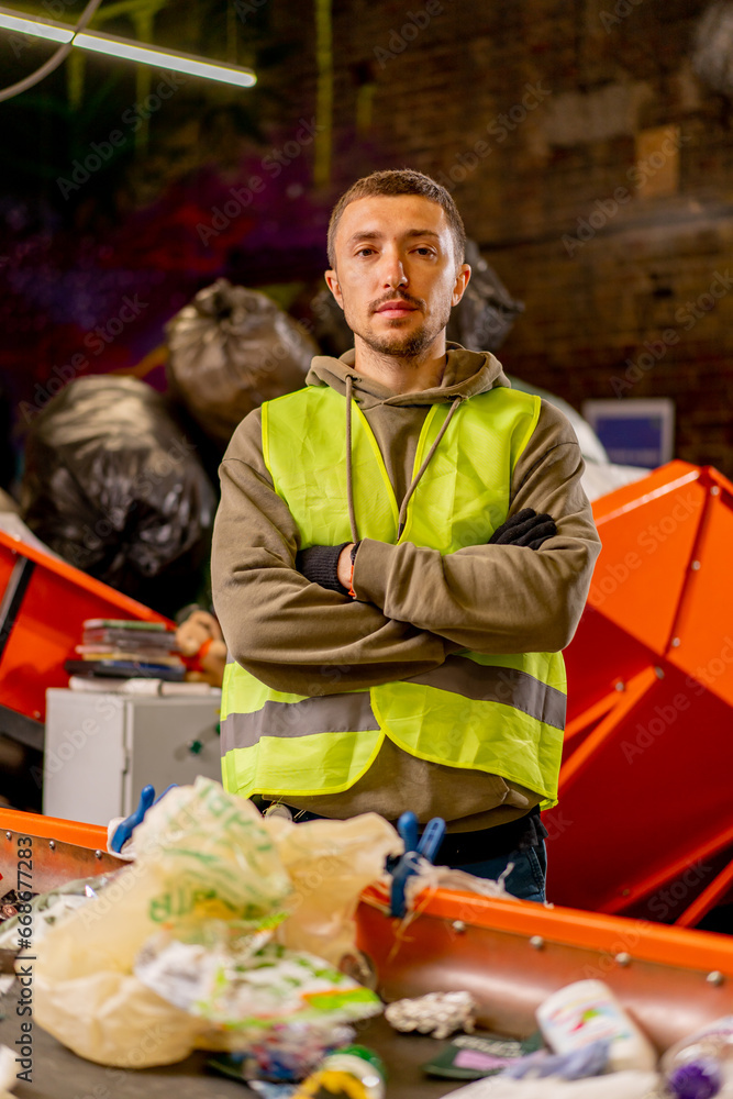 Portrait of a serious man in a protective vest with his arms crossed in front of him and looking at camera at a waste plant