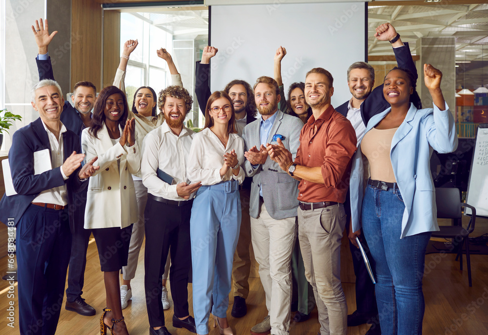 Portrait of diverse excited happy business people standing in office applauding and looking cheerful at the camera. Group of coworkers men and women smiling indoors. Team work concept. - obrazy, fototapety, plakaty 
