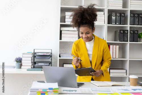 Beautiful young African American accountant working with annual report to calculate taxes and giving online consultation in office, online consulting concept with laptop, video conference,