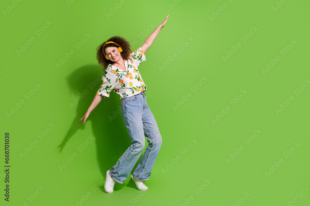 Full length photo of sweet adorable lady wear print shirt having fun enjoying songs earphones empty space isolated green color background Full length photo of sweet adorable lady wear print shirt having fun enjoying songs earphones empty space isolated green color background
