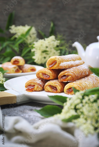 Fripons, French pastries. Apricot jam puff pastry rolls for summer tea and white flowers