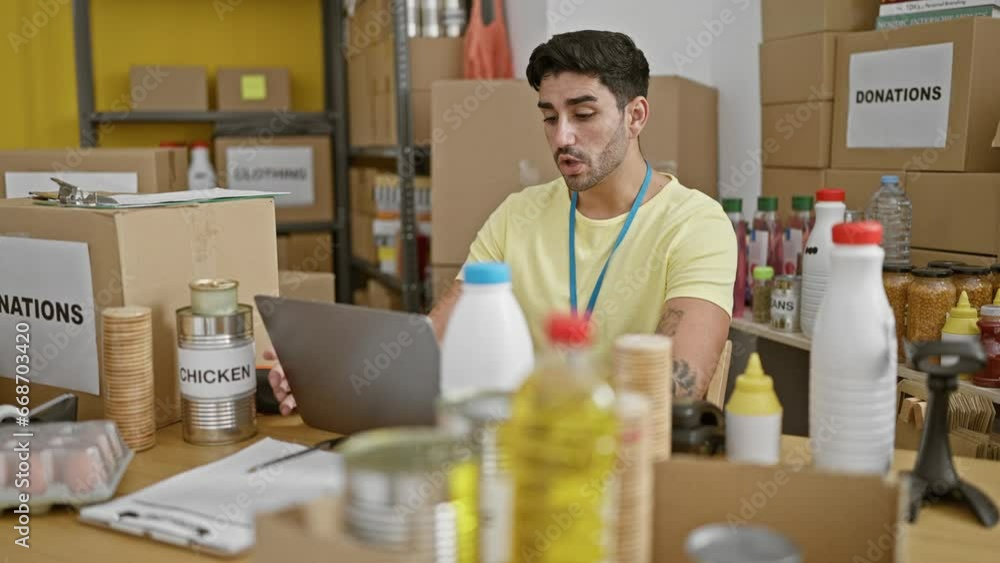 Young hispanic man volunteer having video call sitting on table at charity center Young hispanic man volunteer having video call sitting on table at charity center