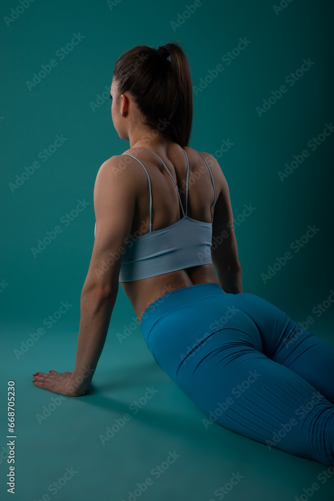 Confident fitness model inspires with powerful body exercises. Fit girl trains in studio, showcasing muscular physique. Turquoise background adds vibrancy. Confident fitness model inspires with powerful body exercises. Fit girl trains in studio, showcasing muscular physique. Turquoise background adds vibrancy.