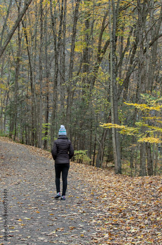 woman walking on a hiking trail in Taughannock Falls State Park (waterfall, cayuga lake near ithaca, upstate new york) in autumn with fall foliage (leaves changing colors) wearing brown jacket, hat © Yuriy T