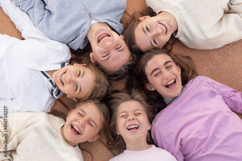 A group of six happy girls lying on their backs  laughing  and enjoying. Happy childhood. Friends forever. Photo taken from above