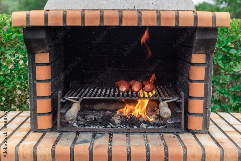 Brick barbecue with sausages sizzling over the fiery charcoal. Party and celebration with friends Brick barbecue with sausages sizzling over the fiery charcoal. Party and celebration with friends