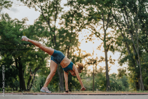 Fit girl performing cartwheel exercises in a green park, showcasing strength, flexibility, and athleticism. Motivating and inspiring examples of a healthy lifestyle.