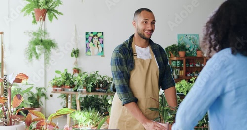 Cheerful handsome young man florist selling flower pot. Woman buys spring housplants in flower store. People in flower shop, client pushing cart. Buyer talking to sales gardener in greenhouse. photo