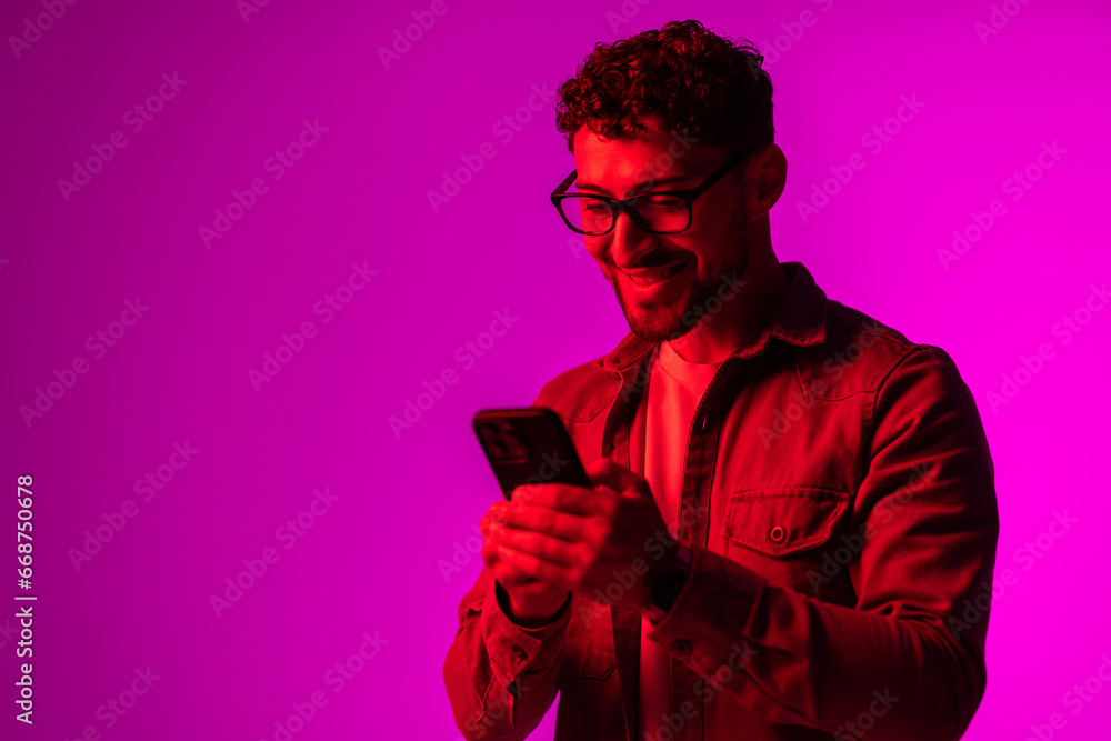 Side view of astonished surprised man in shirt using online service on mobile phone on neon light background. Side view of astonished surprised man in shirt using online service on mobile phone on neon light background.