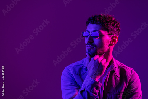Studio shot of handsome young man in stylish sunglasses isolated on g pink background in neon light.