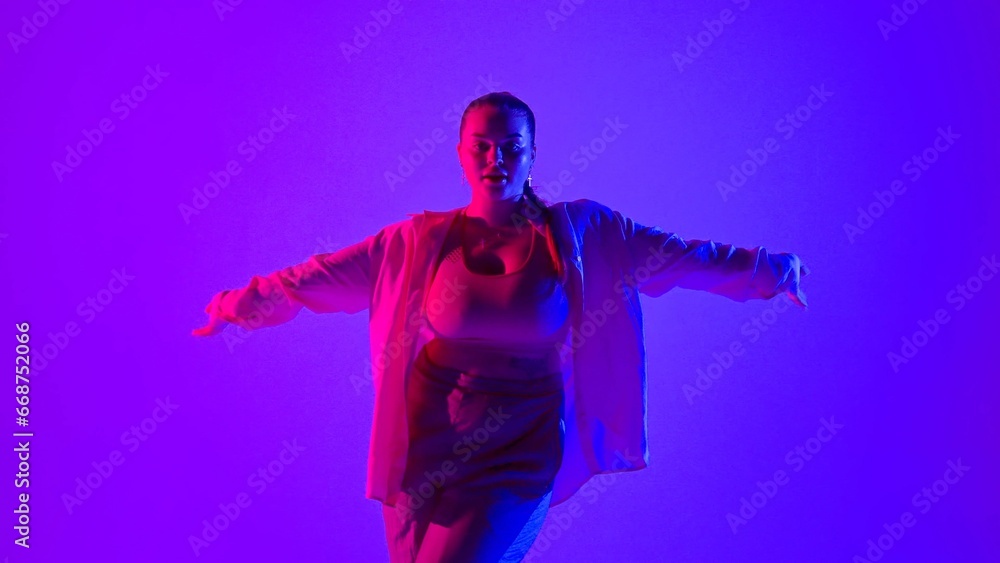 Obraz premium Attractive woman dancing jazz-funk in pink and blue neon light in a studio. Modern dynamic and energetic dance choreography. Medium full.