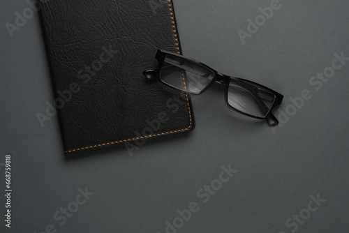 Notebook with black leather cover and eyeglasses on dark gray background. Business concept. Top view. Flat lay