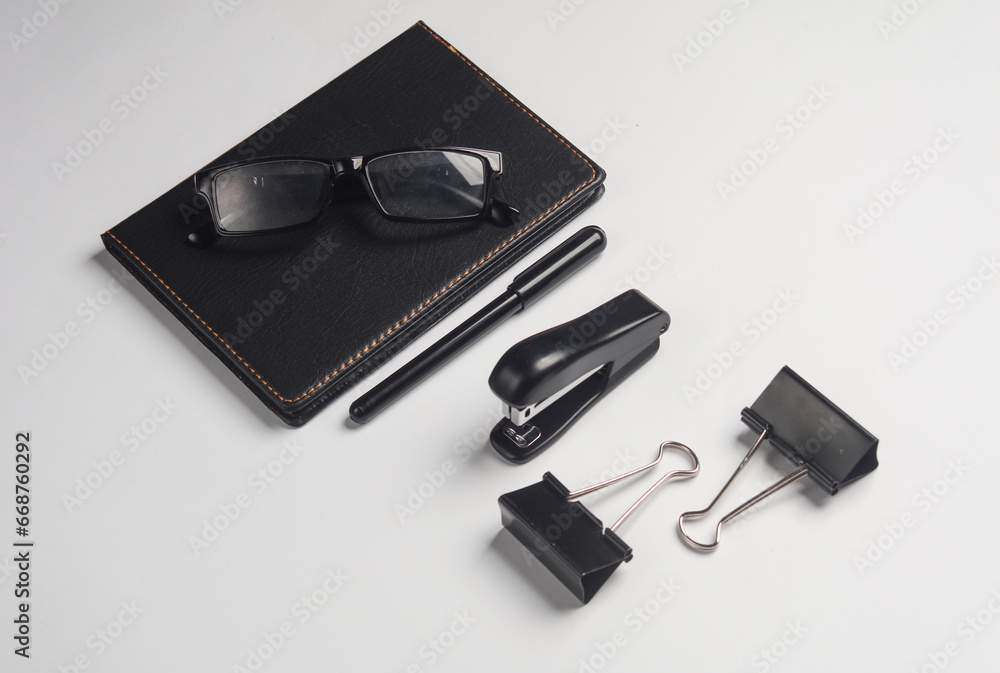 Notebook, stapler, eyeglasses, binders on dark gray background. Black stationery objects Notebook, stapler, eyeglasses, binders on dark gray background. Black stationery objects