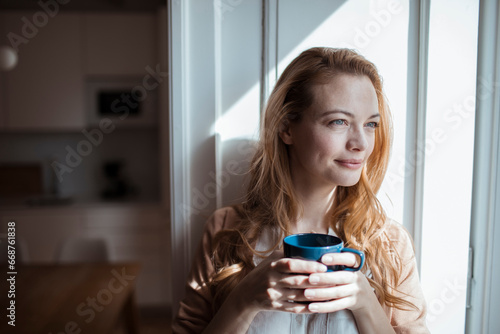 Young woman looking out the window while having coffee at home photo