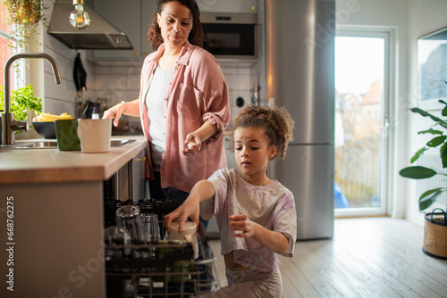 Little girl helping her mother with the dishes in the kitchen photo
