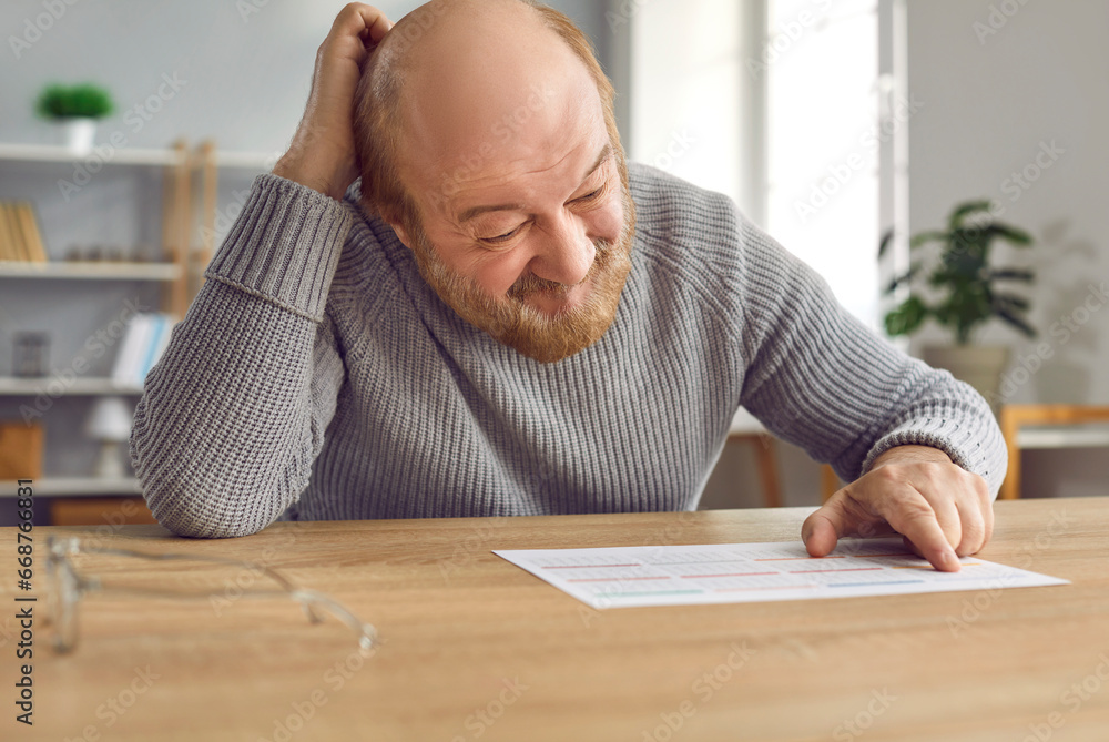 Senior man with dementia gets confused and scratches head when he looks at calendar on table. Old man with Alzheimer's disease can't remember important dates, events, birthdays, hospital appointments Senior man with dementia gets confused and scratches head when he looks at calendar on table. Old man with Alzheimer's disease can't remember important dates, events, birthdays, hospital appointments