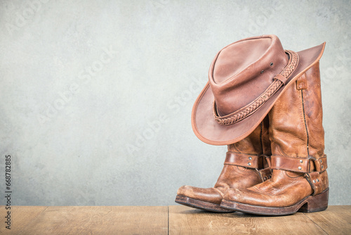Vintage cowboy hat and old leather Wild West boots front concrete wall background. Retro style filtered photo photo