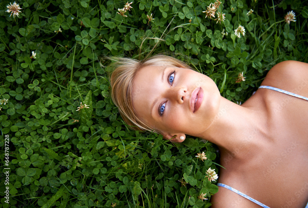 Fototapeta premium Spring, thinking and relax with woman on grass in nature for calm, environment and peace. Park, flowers and field with face of female person lying in countryside for summer, vacation and wellness