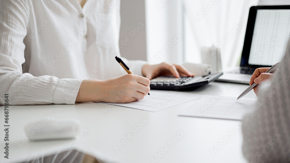 Two accountants using a laptop computer and calculator for counting taxes at white desk in office. Teamwork in business audit and finance Two accountants using a laptop computer and calculator for counting taxes at white desk in office. Teamwork in business audit and finance