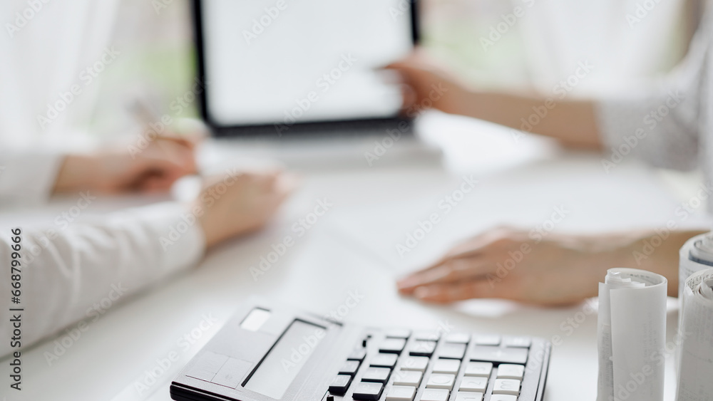 Fototapeta premium Calculator is lying at the white table near two female accounters counting taxes or making revenue balance. Business audit and finance concepts