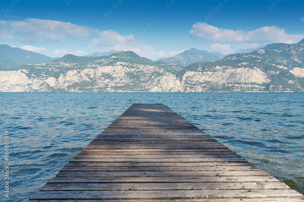 Holzsteg am Ufer des Gardasee bei Malcesine in Italien. Am Horizont Berge der Alpen