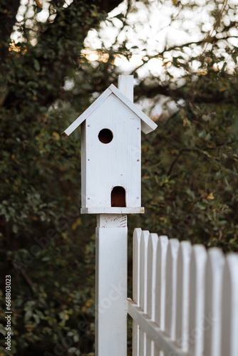 A white birdhouse on a wooden fence in the courtyard of a private house.
