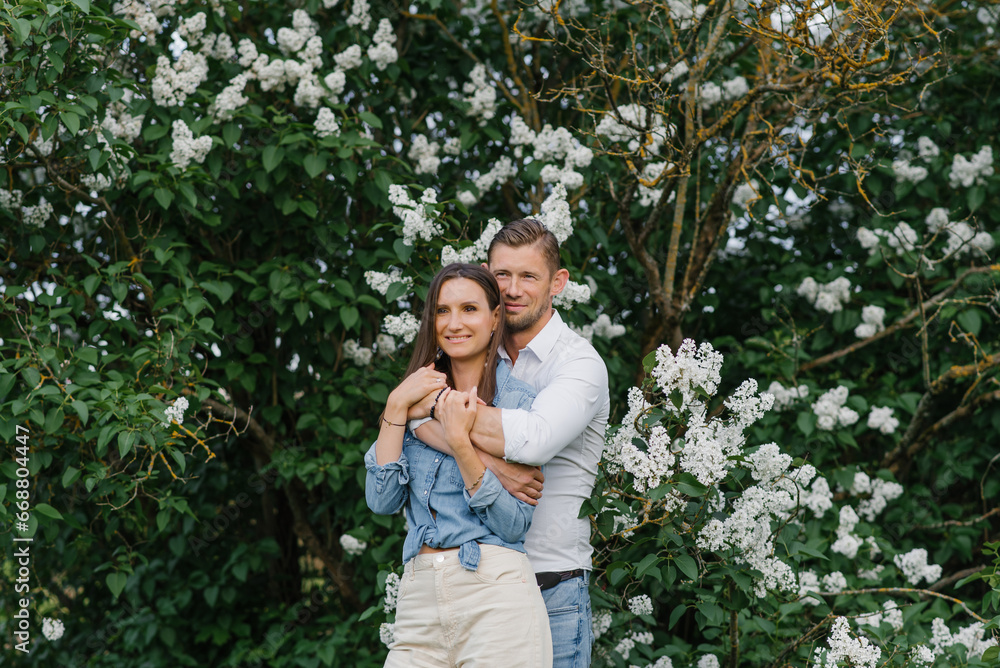 Beautiful young couple in a romantic place, spring blooming lilac garden. Happy joyful couple enjoying each other while walking in the garden Beautiful young couple in a romantic place, spring blooming lilac garden. Happy joyful couple enjoying each other while walking in the garden