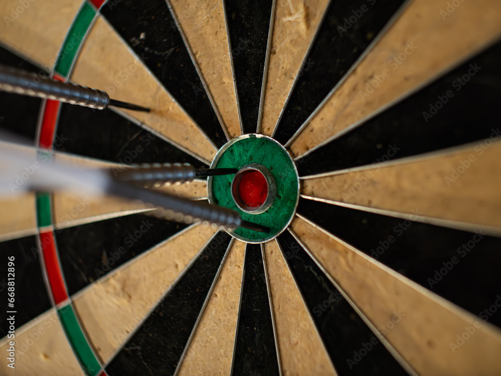 Darts in a dartboard close up. The bullseye is the target but it was missed. The objective is to hit the center. This leisure activity is a popular game in a pub. Darts in a dartboard close up. The bullseye is the target but it was missed. The objective is to hit the center. This leisure activity is a popular game in a pub.