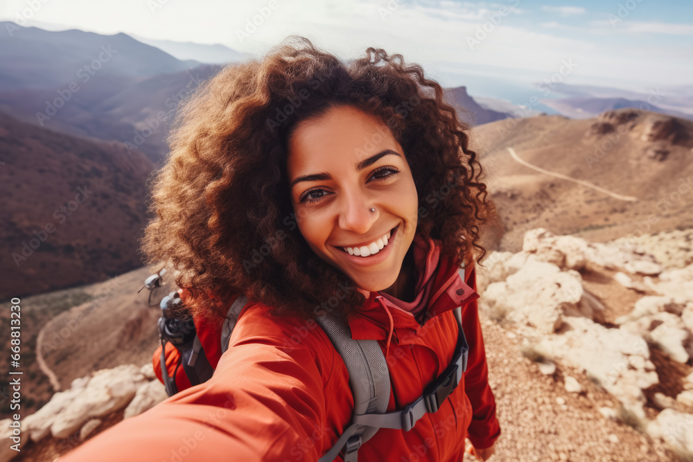 Young arab hiker woman taking a selfie portrait on the top of a mountain. Happy young athletic woman on adventure, taking a photo with beautiful view