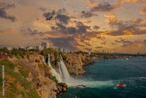 The moment when the Lower Düden waterfall flows into the sea, against the background of the steep shores of the Mediterranean and the urban development of the city of Antalya.