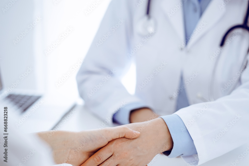 Doctor and patient shaking hands while sitting opposite of each other at the table in clinic, just hands close up. Medicine concept Doctor and patient shaking hands while sitting opposite of each other at the table in clinic, just hands close up. Medicine concept
