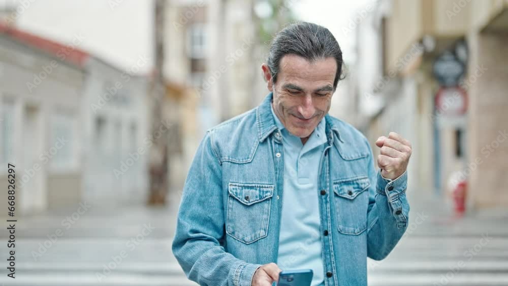 Middle age man using smartphone celebrating at street Middle age man using smartphone celebrating at street