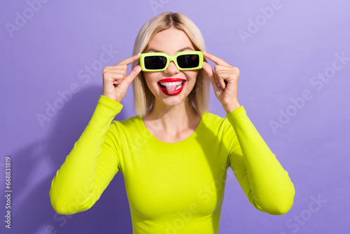 Portrait of good mood woman with bob hairdo dressed yellow top touch sunglass showing tongue fooling isolated on purple color background