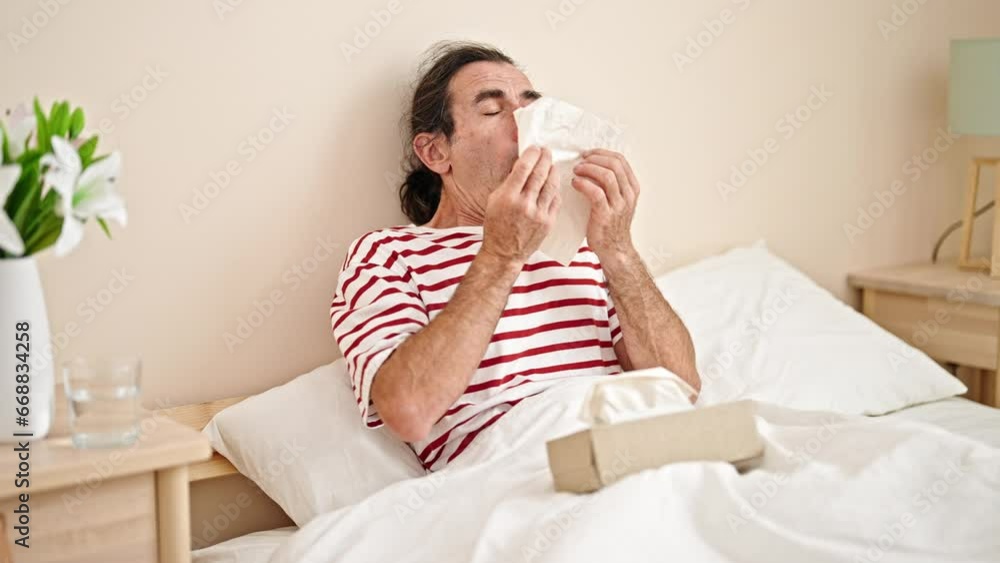 Middle age man sitting on bed sneezing at bedroom Middle age man sitting on bed sneezing at bedroom