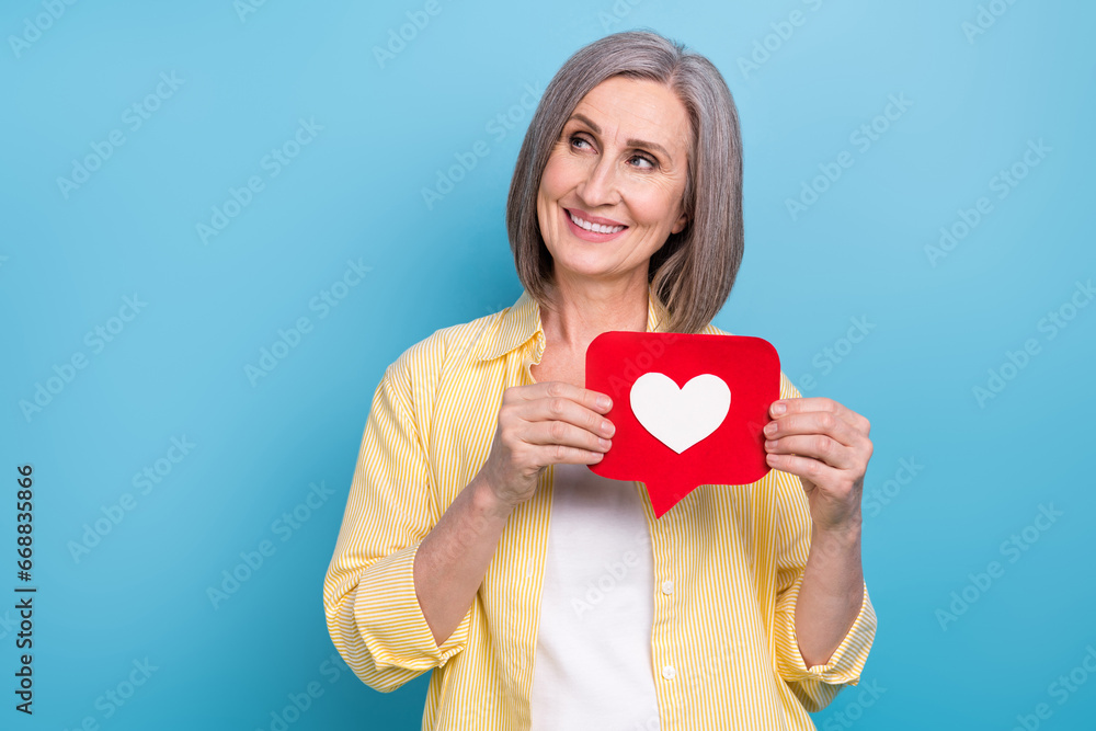 Photo of dreamy shiny woman dressed yellow shirt holding heart like card looking empty space isolated blue color background Photo of dreamy shiny woman dressed yellow shirt holding heart like card looking empty space isolated blue color background