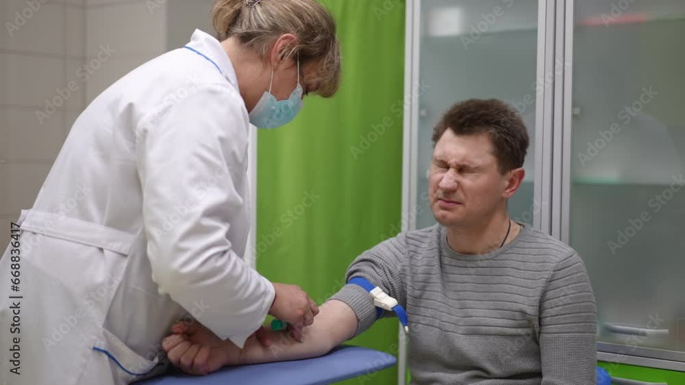A female health worker in a clinic, makes a painful puncture in the vein of a male patient's right arm to take blood for analysis A female health worker in a clinic, makes a painful puncture in the vein of a male patient's right arm to take blood for analysis
