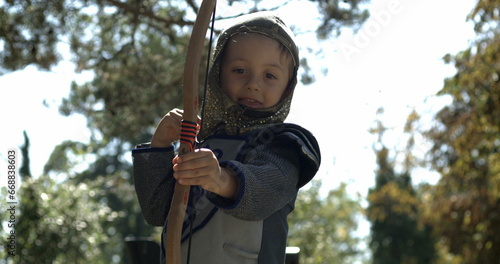 Small boy wearing medieval costume throwing arrow holding bow outside captured