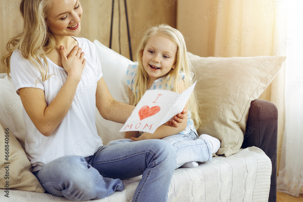 Happy mother day in sunny flat. Child daughter congratulates mom and gives her postcard with heart drawing. Family concept Happy mother day in sunny flat. Child daughter congratulates mom and gives her postcard with heart drawing. Family concept