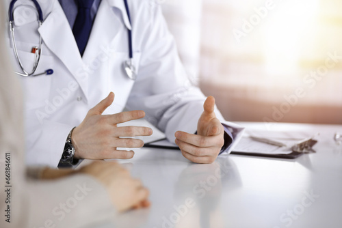 Unknown male doctor and patient woman discussing something while sittingin a darkened clinic, glare of light on the background. Close-up of hands photo