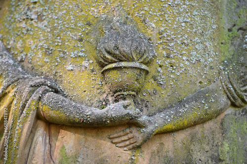 Partial view to a weathered sandstone sculpture on a graveyard which shows to hands holding the eternal fire. photo