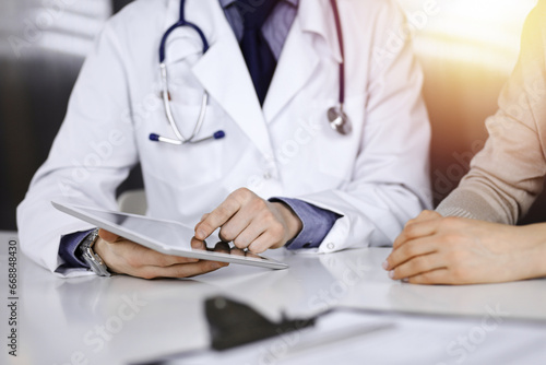 Unknown male doctor and patient woman discussing something while using tablet computer in a darkened clinic  glare of light on the background. Best medical service in hospital  medicine  pandemic stop