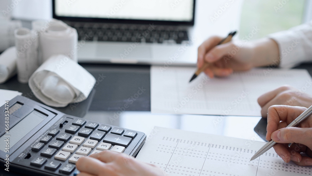 Two accountants use a calculator and laptop computer for counting taxes or revenue balance. Business, audit, and taxes concepts Two accountants use a calculator and laptop computer for counting taxes or revenue balance. Business, audit, and taxes concepts