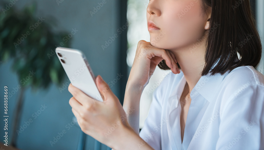 スマートフォンを見て悩むビジネスウーマン スマートフォンを見て悩むビジネスウーマン