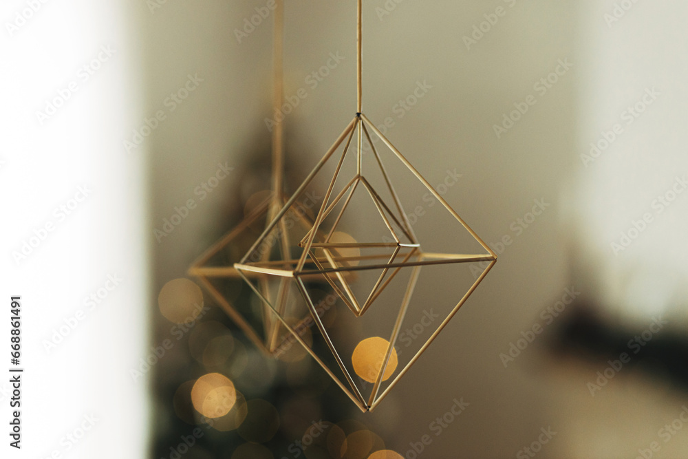 Decorating home with christmas straw spiders. Rustic nordic straw decoration hanging on background of festive golden lights bokeh in modern farmhouse living room. Holiday traditions