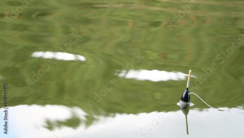 A black and white float on the surface of the lake on a sunny summer day. Fishing tackle made of plastic in the reflection on the surface of the water.