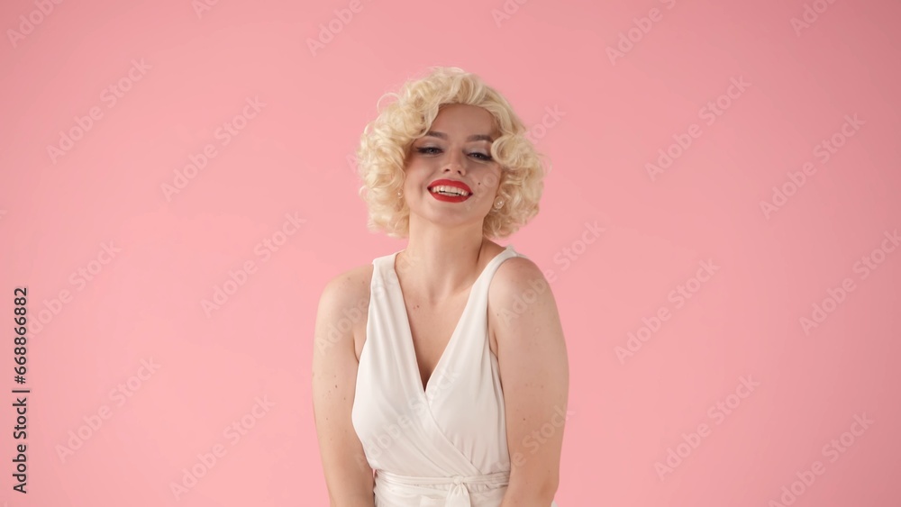 Portrait young woman in wig, white dress and with red lipstick on lips in studio on pink background. Woman looking like Marilyn Monroe in studio on pink background.