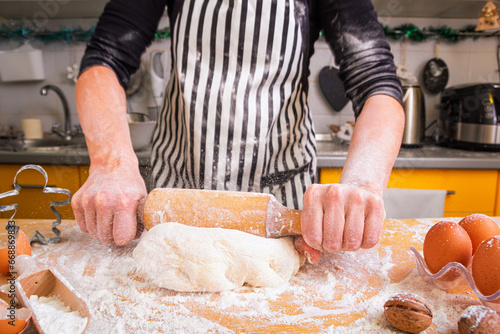 Woman confectioner in a striped culinary apron rolls the dough while making homemade baking, close up