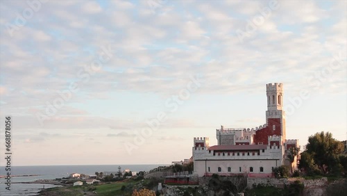 portopalo sicily italy red white castle shot from side next to water with clouds sky above, wide shot