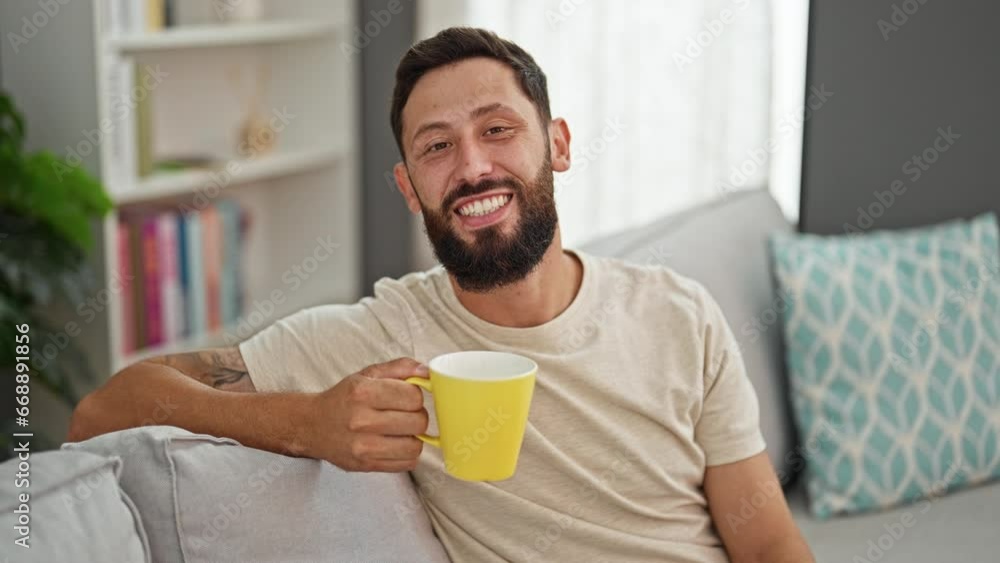 Young hispanic man drinking coffee sitting on sofa at home Young hispanic man drinking coffee sitting on sofa at home