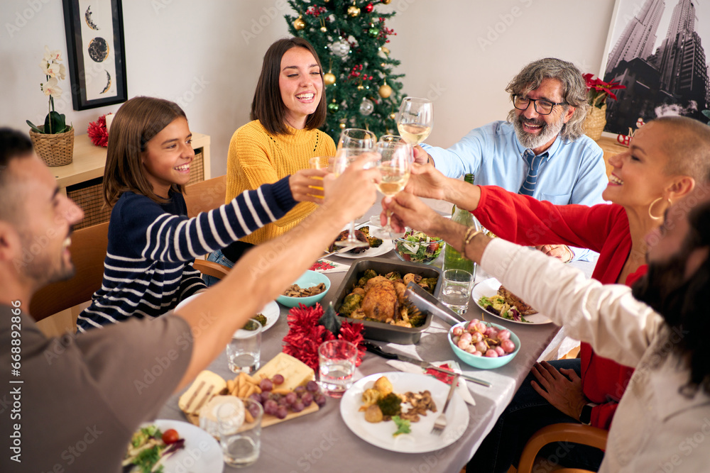 Cheerful European people toasting with white wine at Christmas gathering. Smiling Caucasian family celebrating Christmas vacations together at festive table. Generations enjoying domestic life. 